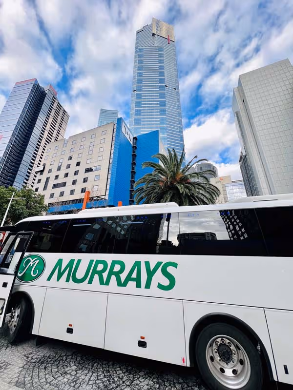 Image of a Murrays Coach in the Melbourne City with the city skyline in the background.